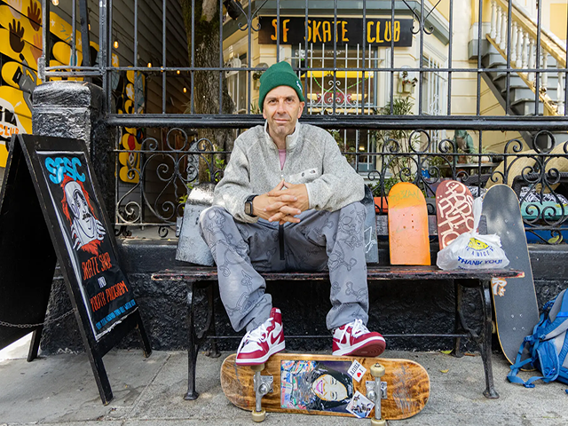 A man sitting in a bench with his feet resting on a skateboard