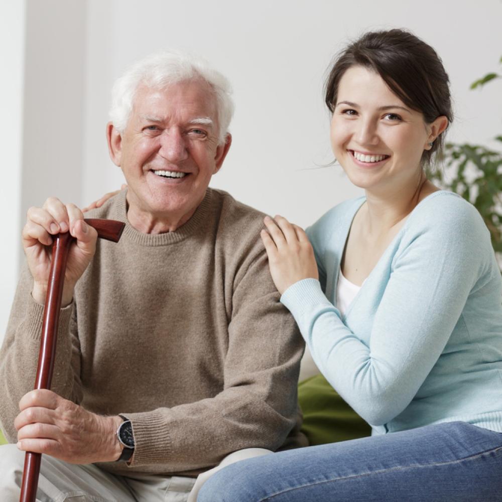 An image of a smiling elderly man holding a cane and a smiling young woman
