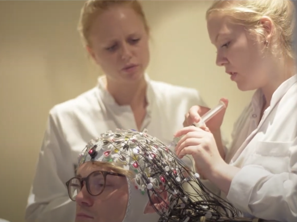 Two scientists are fittiing an EEG cap on a patient who is seated 