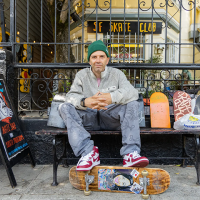 A man sitting on a bench in San Francisco with his feet on a skateboard