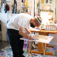 A man bending over a canvas with a thick silver marker in his hand